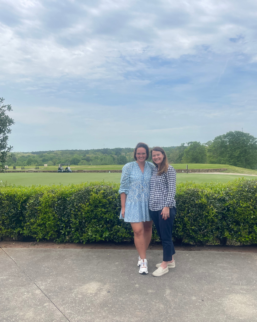 Two women standing in front of a scenic golf course, representing teamwork and collaboration for Pinterest management success.